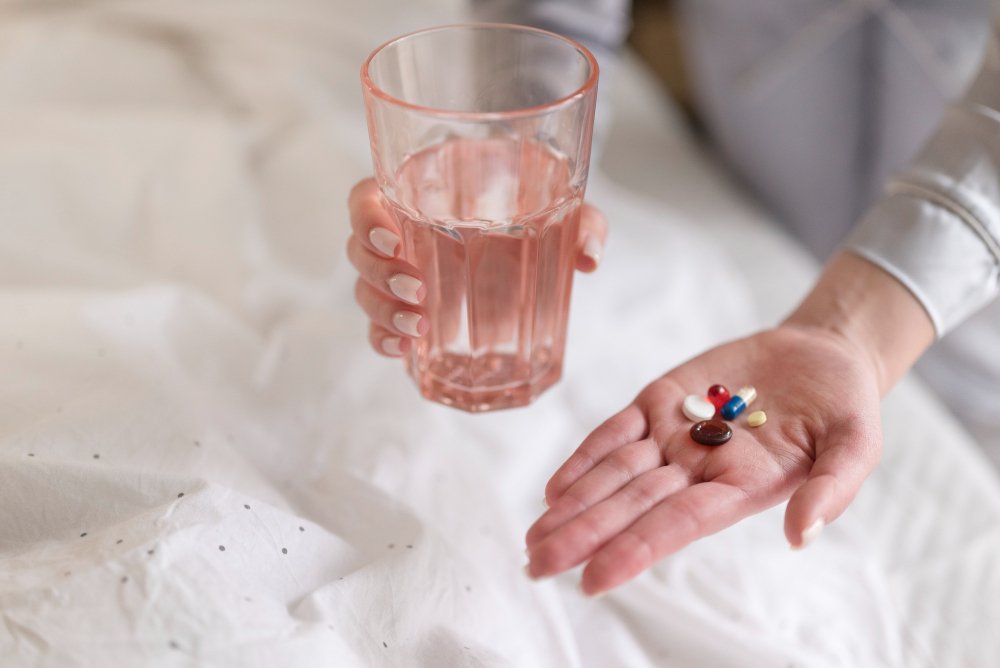 a person holding a glass of water and pills.	